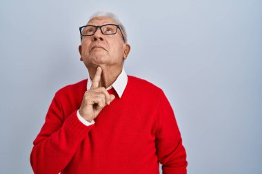Senior man with grey hair standing over isolated background thinking concentrated about doubt with finger on chin and looking up wondering 