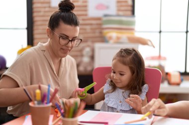 Teacher and toddler smiling confident cutting paper at kindergarten