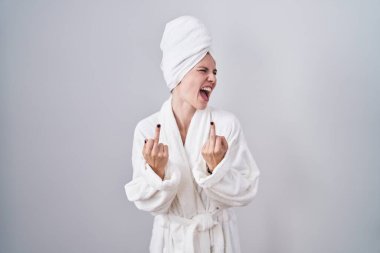 Blonde caucasian woman wearing bathrobe showing middle finger doing fuck you bad expression, provocation and rude attitude. screaming excited 