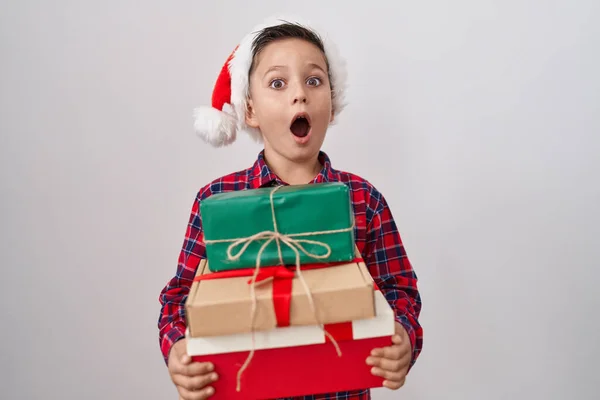 Little Hispanic Boy Wearing Christmas Hat Holding Presents Afraid Shocked — Stok fotoğraf