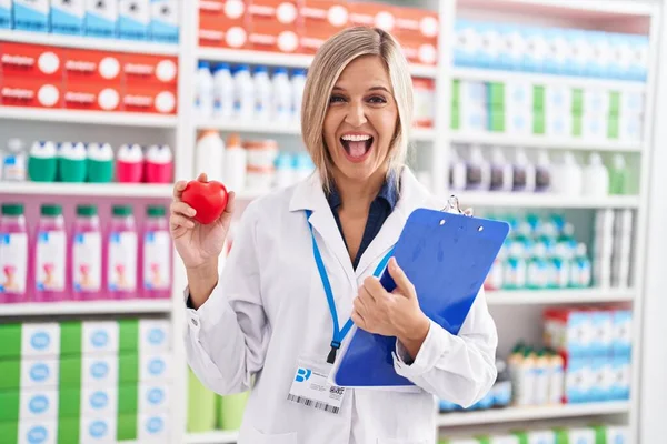 Young Woman Working Pharmacy Drugstore Holding Heart Smiling Laughing Hard — Stock Photo, Image