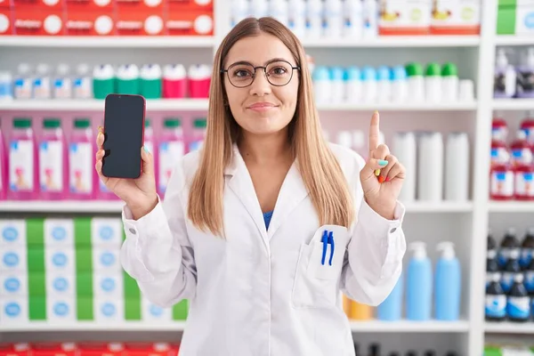 Young Blonde Woman Working Pharmacy Drugstore Showing Smartphone Screen Smiling — Stockfoto