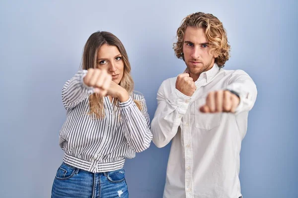 Young Couple Standing Blue Background Punching Fist Fight Aggressive Angry — Zdjęcie stockowe