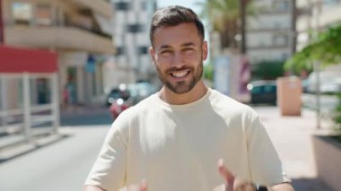 Young hispanic man smiling confident doing ok sign with thumbs up at street