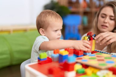 Teacher and toddler playing with construction blocks sitting on table at kindergarten