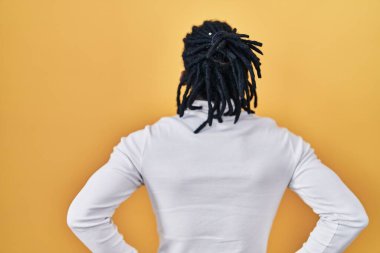 Sarı arka planda balıkçı yaka kazak giyen Afrikalı adam kolları vücudunda geriye doğru bakıyor. 