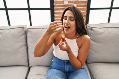 Genç İspanyol kadın evdeki kanepede oturmuş şurup içiyor.
