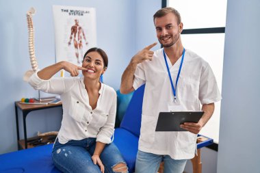 Fizyoterapist randevusundaki genç İspanyol kadın neşeli bir şekilde gülümseyip parmaklarını ve ağzını gösterdi. diş sağlığı kavramı. 