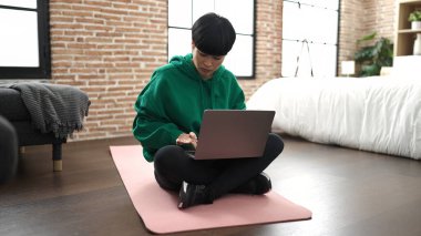 Young chinese woman using laptop sitting on floor at bedroom