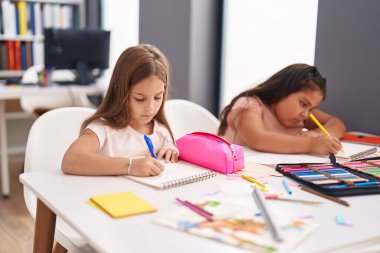 Two kids preschool students sitting on table drawing on paper at classroom