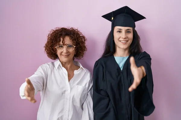 卒業キャップと式のローブを着たヒスパニック系の母親と娘は 挨拶や歓迎として握手を提供して笑顔 成功したビジネス — ストック写真