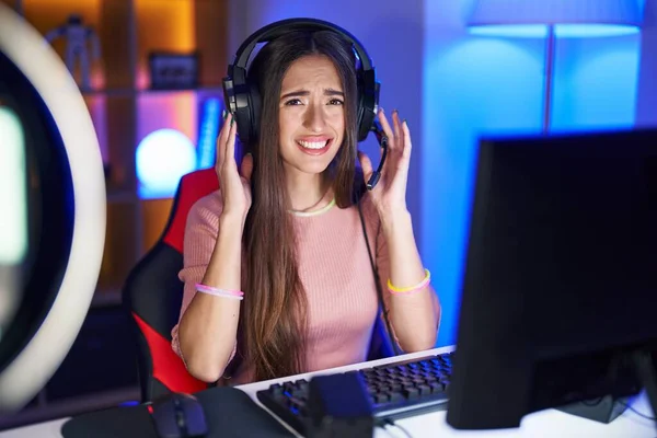 Young hispanic woman playing video games covering ears with fingers with annoyed expression for the noise of loud music. deaf concept.