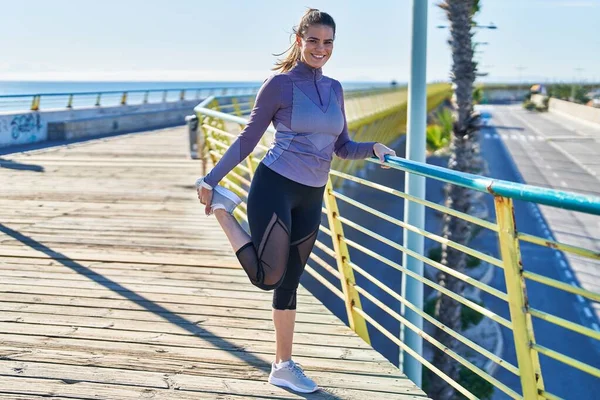 Young Beautiful Hispanic Woman Wearing Sportswear Stretching Leg Seaside — Stockfoto