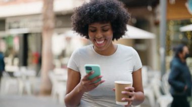 Genç Afrikalı Amerikalı kadın akıllı telefon kullanıyor. Sokakta kahve içiyor.