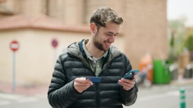 Genç adam caddede akıllı telefon ve kredi kartı kullanıyor.