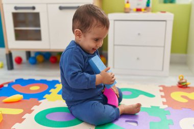Tapılası İspanyol çocuk anaokulunda yerde kendinden emin bir şekilde otururken gülümsüyor.