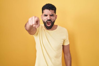 Hispanic man with beard standing over yellow background pointing displeased and frustrated to the camera, angry and furious with you 