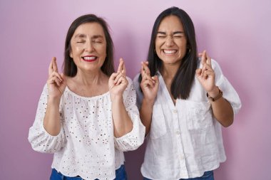Hispanic mother and daughter together gesturing finger crossed smiling with hope and eyes closed. luck and superstitious concept. 