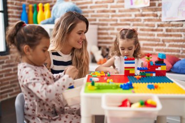 Teacher with girls playing with construction blocks sitting on table at kindergarten