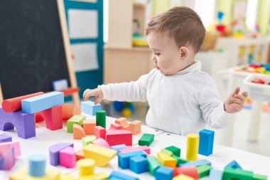 Sevimli beyaz bebek anaokulunda duran inşaat bloklarıyla oynuyor.