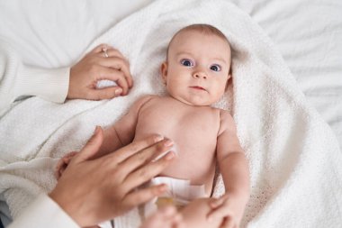 Adorable caucasian baby lying on bed applying cream on body skin at bedroom