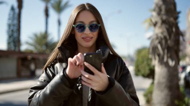 Parkta akıllı telefon kullanarak gülümseyen güzel bir İspanyol kadın.