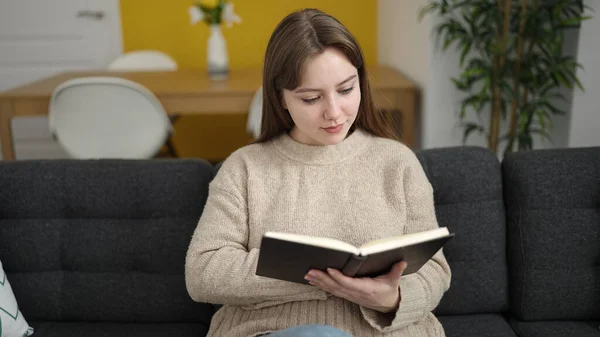 Young Blonde Woman Reading Book Sitting Sofa Home —  Fotos de Stock