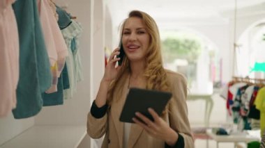 Genç sarışın tezgahtar akıllı telefondan konuşuyor. Elbise mağazasında dokunmatik ped kullanıyor.