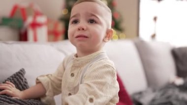 Evdeki üzgün ifadeyle Noel ağacının yanındaki koltukta oturan sevimli bebek.