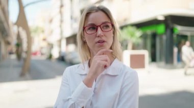 Sokakta şüpheli bir ifadeyle duran genç sarışın kadın.