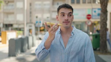 Genç İspanyol adam gülümsüyor. Akıllı telefonla konuşuyor. Sokakta yürüyor.