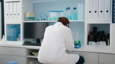 Laboratuvarda mikroskop kullanan orta yaşlı kadın bilim adamı üniforması giyiyor.