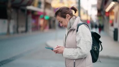 Sokakta akıllı telefon kullanan orta yaşlı bir kadın gülümsüyor.
