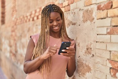 Afro-Amerikalı kadın, izole taştan arka planda akıllı telefon kullanarak gülümsüyor.