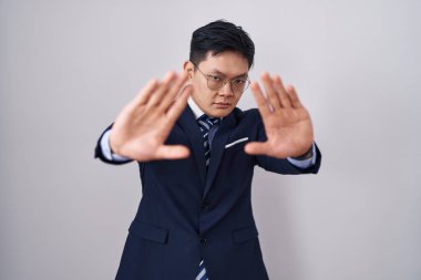 Young asian man wearing business suit and tie doing frame using hands palms and fingers, camera perspective 