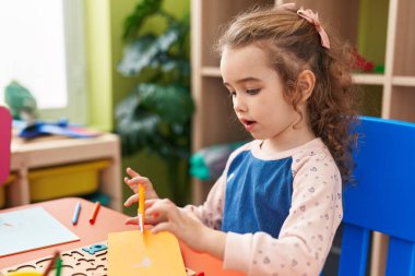 Adorable blonde girl student cutting paper at kindergarten