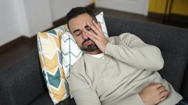 Young hispanic man lying on sofa with worry expression at home