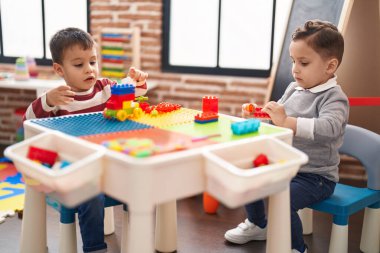 Two kids playing with construction blocks sitting on table at kindergarten