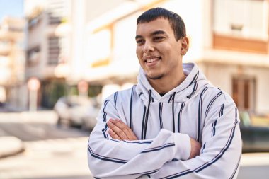 Genç adam kendinden emin gülümsüyor. Kollarını kavuşturup caddede hareketler yapıyor.