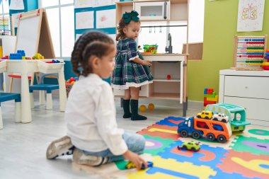 Brother and sister playing with cars toy sitting on floor at kindergarten