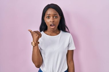 Gündelik beyaz tişört giyen Afrikalı genç bir kadın elleri yana dönük, ağzı açık şaşkın bir ifadeyle şaşırdı.. 