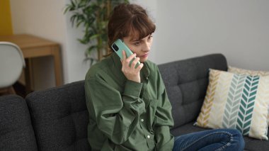Young caucasian woman talking on the phone with disgust at home