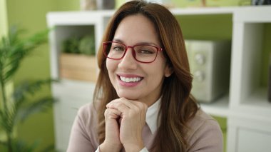 Young beautiful hispanic woman smiling confident sitting on table at home
