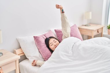 Chinese woman waking up stretching arms at bedroom
