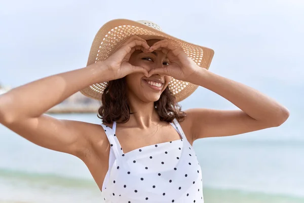 若いですアフリカ系アメリカ人女性身に着けています夏の帽子行います心ジェスチャーとともに手で海辺 — ストック写真