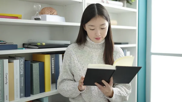 Young chinese woman student reading book studying at library university