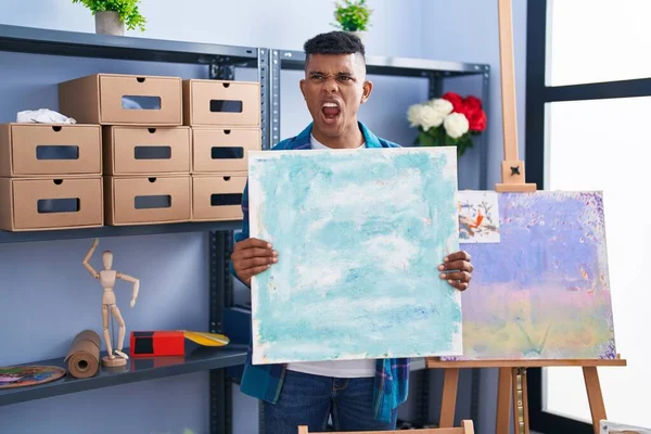 アーティスト スタジオでキャンバスを持っている若いヒスパニック系の男は怒りと怒りで叫んで フラストレーションと激怒叫んで怒っています 怒りと攻撃的な考え方 — ストック写真