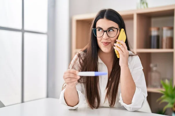 Młoda Brunetka Trzyma Wynik Testu Ciążowego Rozmawiając Przez Telefon Uśmiechając — Zdjęcie stockowe