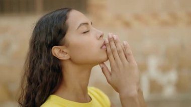 Young african american woman praying with closed eyes at street