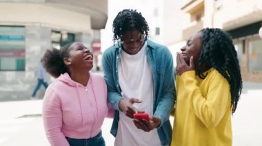 Afro-Amerikalı arkadaşlar yan yana durup akıllı telefondan caddede video izliyorlar.